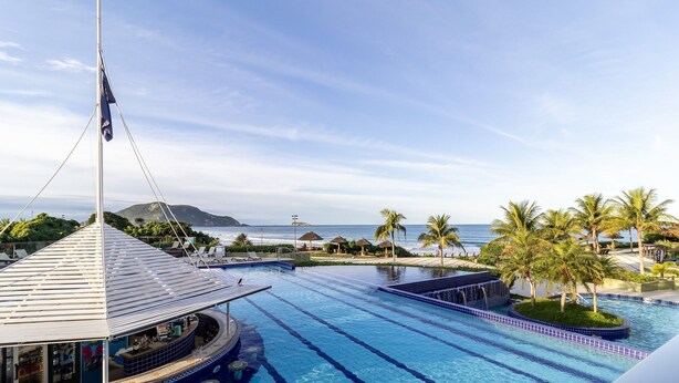 A resort pool with a view of the ocean and palm trees. - Flat Vista mar Dentro de Resort de Luxo Sto2206 (Florianópolis)