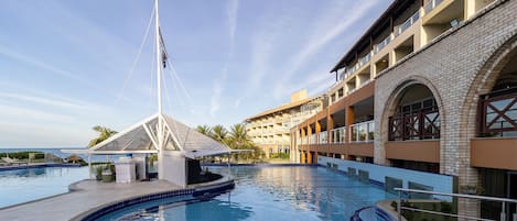 Una piscina con un puente, un edificio con varios balcones y un cielo despejado.