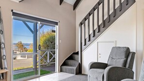 A modern interior with a sliding glass door leading to a balcony, grey upholstered chairs, and a staircase with dark railings.
