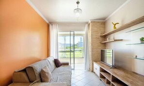 A modern living room with a sofa, TV, and a balcony with a view.