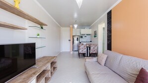 Una sala de estar moderna con un televisor de pantalla plana, estanterías de madera, un sofá y un comedor al fondo.