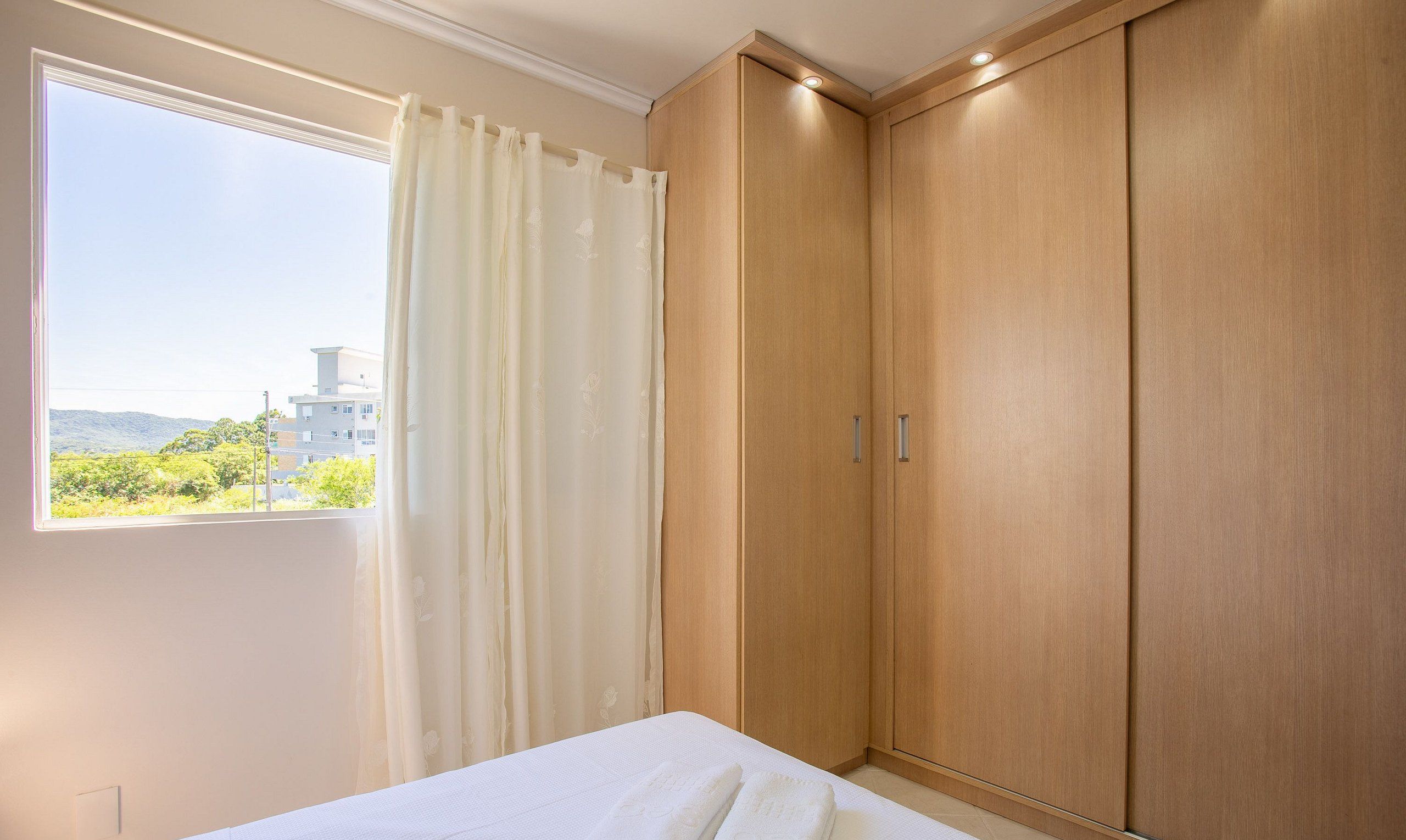 Un dormitorio con cama, ventana con cortinas y armarios de madera.