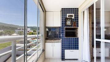 A balcony with a glass railing, a small kitchen area with blue tiles, and a view of a residential area.