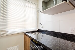 Een moderne keuken met een zwart granieten aanrechtblad, een roestvrijstalen spoelbak en een witte tegelachtergrond.