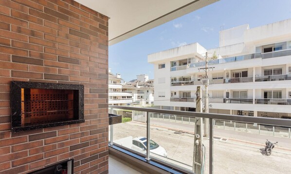 A balcony with a brick wall and a metal railing overlooking a street with parked cars and buildings. - Building With Swimming Pool in Ingleses Norte - STN (Florianópolis)