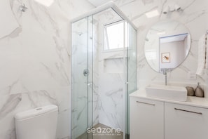 A modern bathroom with a glass-enclosed shower, a white sink, and a marble-tiled wall. - Building With Swimming Pool in Ingleses Norte - STN (Florianópolis)