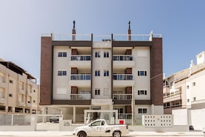 A multi-story residential building with a central entrance, balconies, and a parking area in front. - Building With Swimming Pool in Ingleses Norte - STN (Florianópolis)