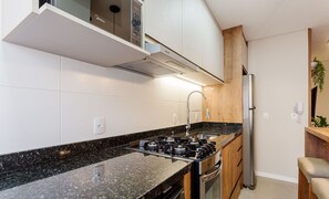 A modern kitchen with a black granite countertop, stainless steel appliances, and wooden cabinetry. - Building With Swimming Pool in Ingleses Norte - STN (Florianópolis)