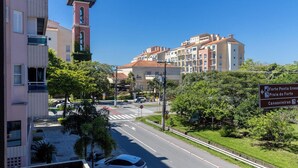 A street view with buildings, a clock tower, and a sign indicating directions to Forte Ponta Grossa, Praia do Forte, and Canasvieiras.