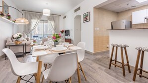 Une cuisine moderne dotée d’un four encastré, un coin repas avec une table et des chaises blanches, et un salon avec un canapé et une table basse.