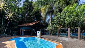Una piscina con cubierta de madera, rodeada de exuberante vegetación y un pequeño pabellón.