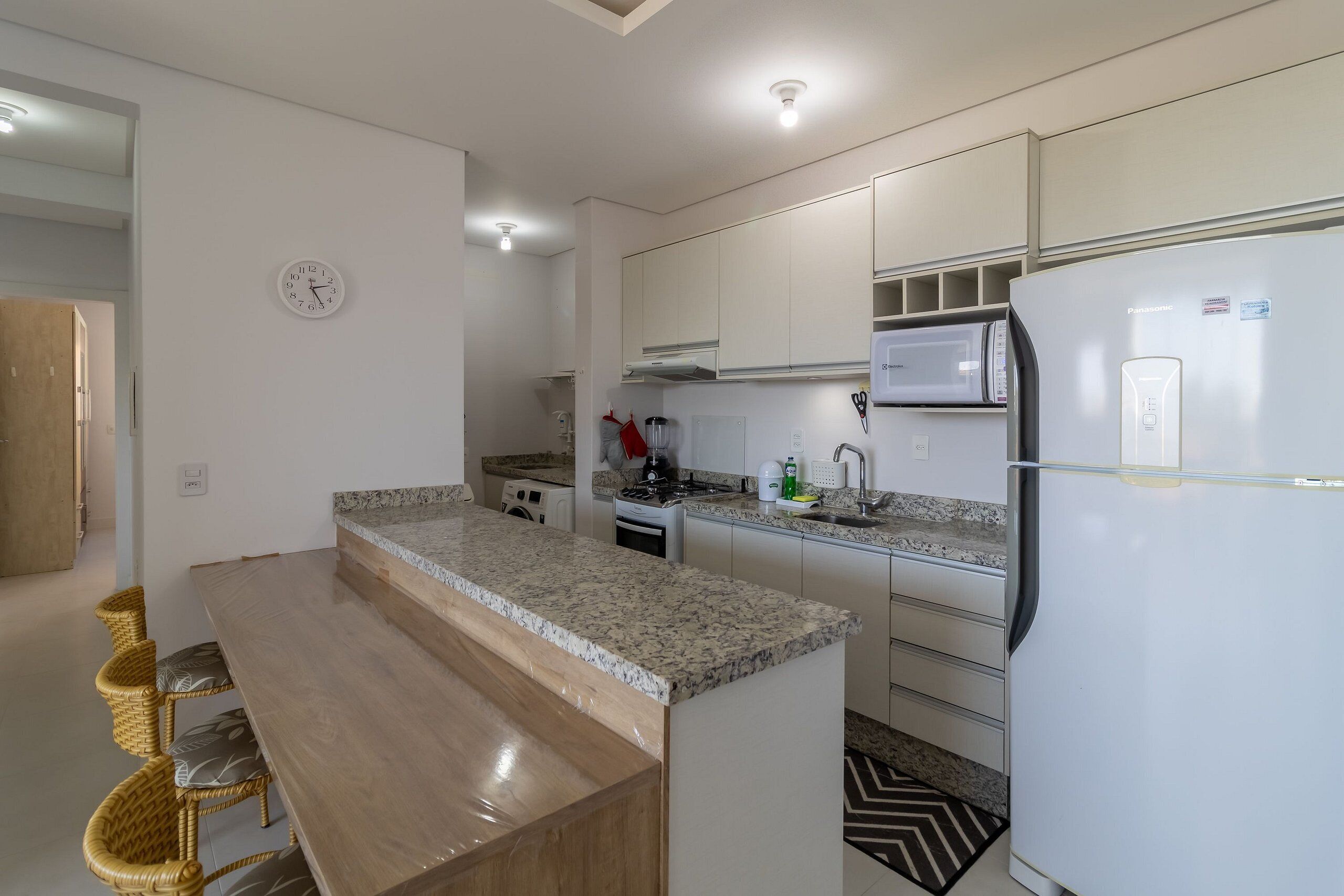 Una cocina moderna con microondas integrado, refrigerador y comedor con mesa de madera y sillas de mimbre.