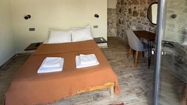 A bedroom with a wooden ceiling, a bed with white linens, a stone wall, and a glass door leading outside. - Casa Küçükköy (Ayvalik)