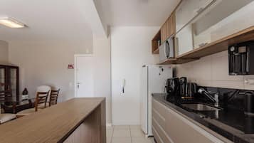A compact kitchen with a refrigerator, microwave, and coffee maker. There is a dining area with a table and chairs.