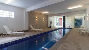 Una piscina interior con paredes de azulejos, una pared decorativa de ladrillo y una zona de estar con sillas y una planta en maceta.