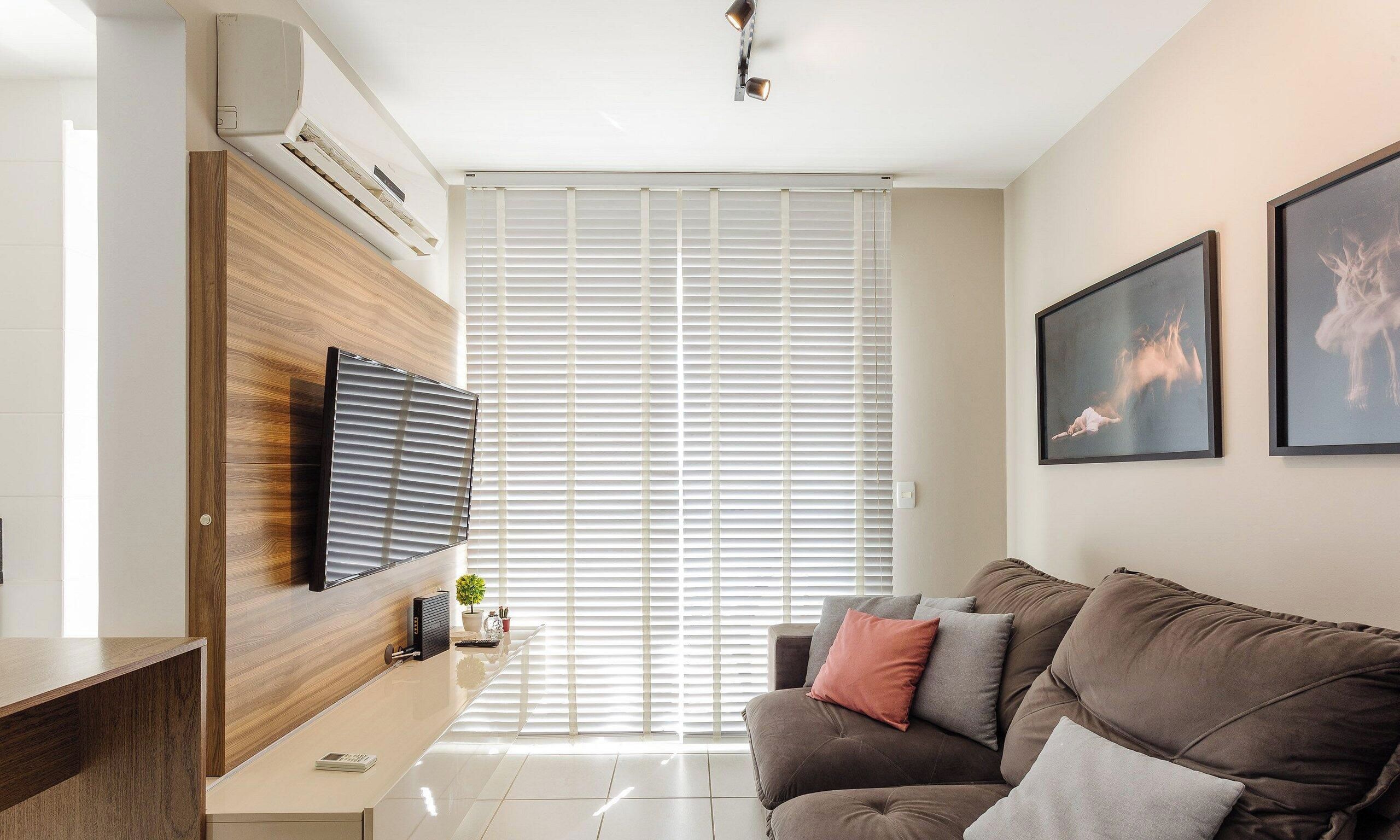 Una sala de estar moderna con un televisor de pantalla plana montado en una pared de madera, un sofá con cojines y un ventanal con persianas.