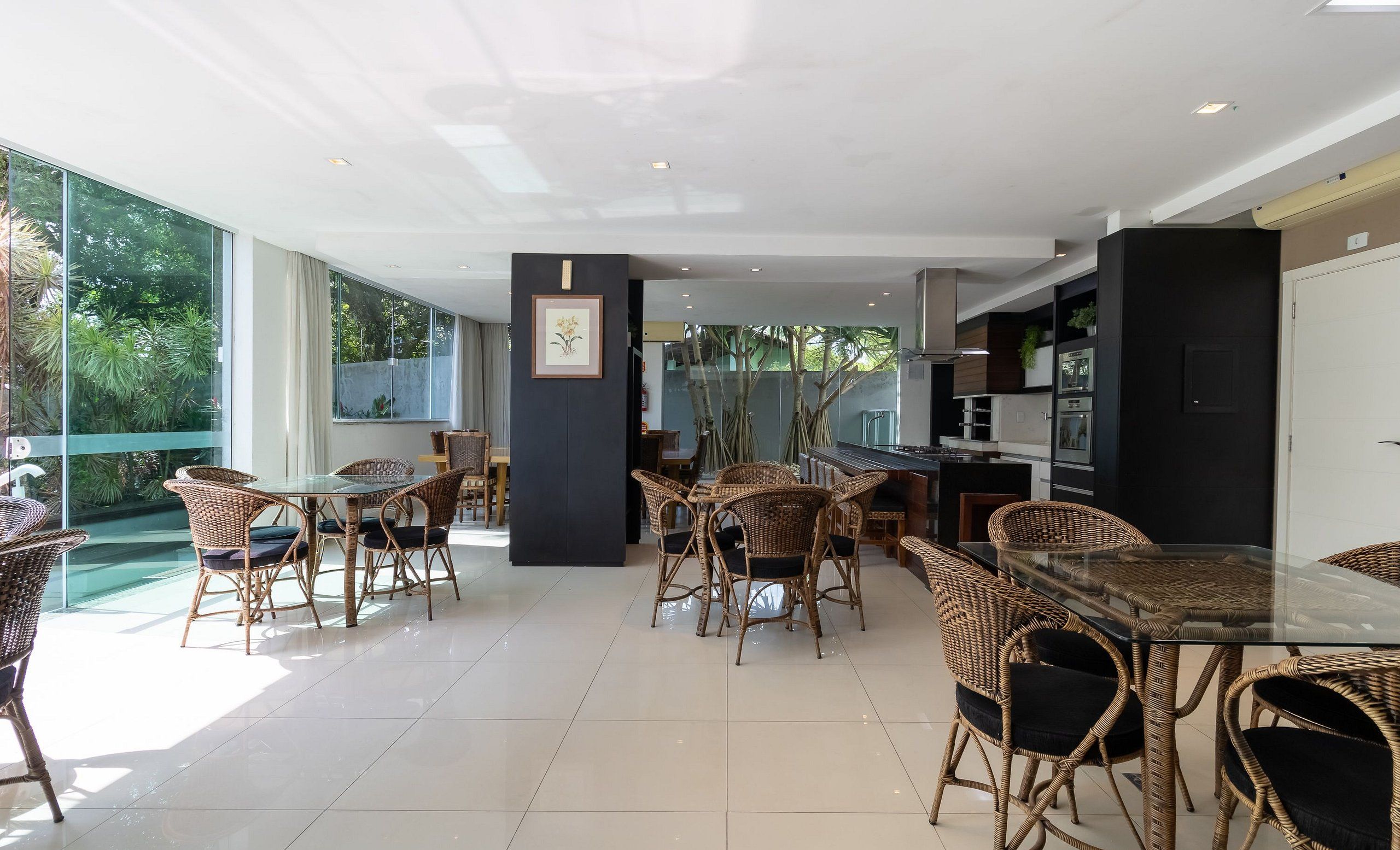 Un espacio interior amplio con muebles de mimbre, una mesa de cristal y una cocina visible a través de puertas de vidrio.