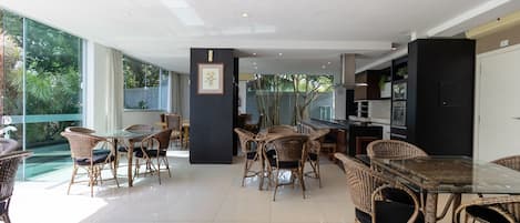 A spacious indoor area with wicker furniture, a glass table, and a kitchen area visible through glass doors.