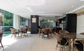 Un espacio interior amplio con muebles de mimbre, una mesa de cristal y una cocina visible a través de puertas de vidrio.