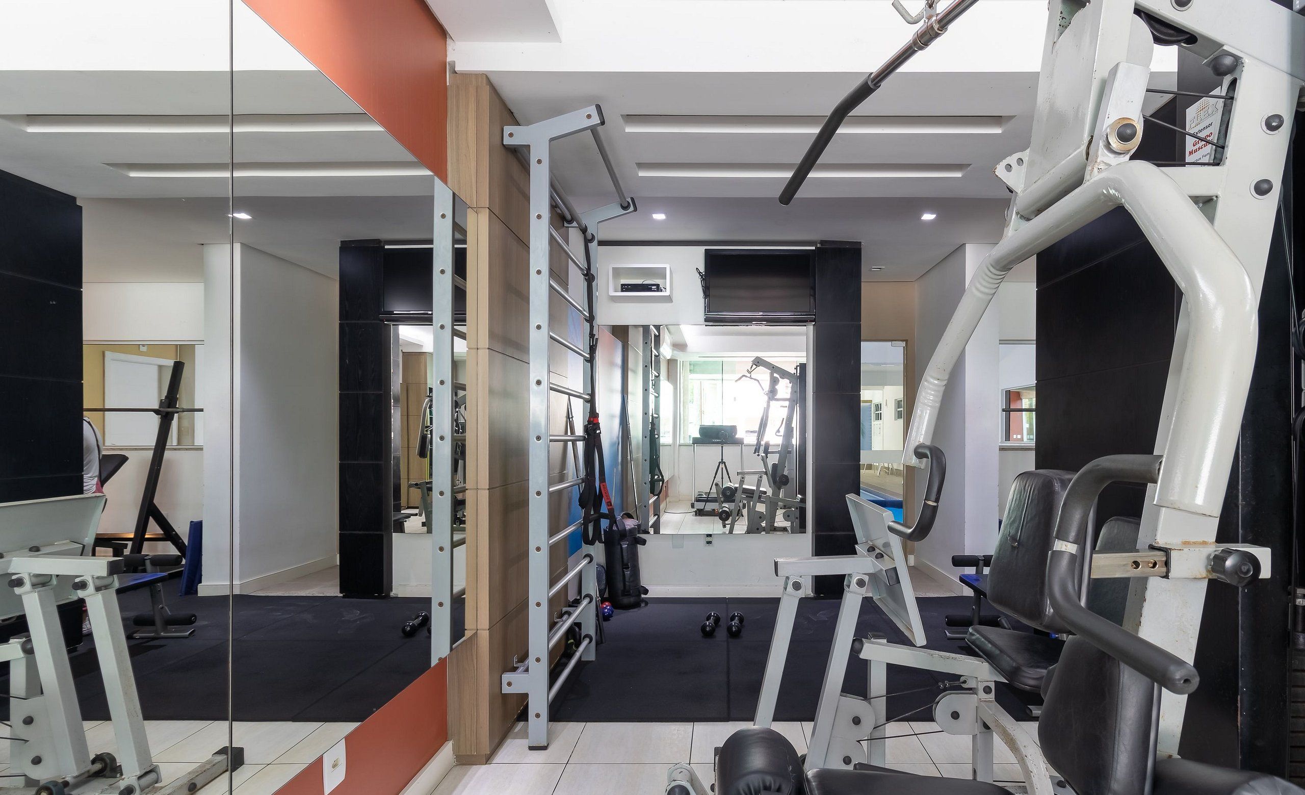 Un gimnasio con equipamiento de ejercicio, espejos y suelo de goma negra.