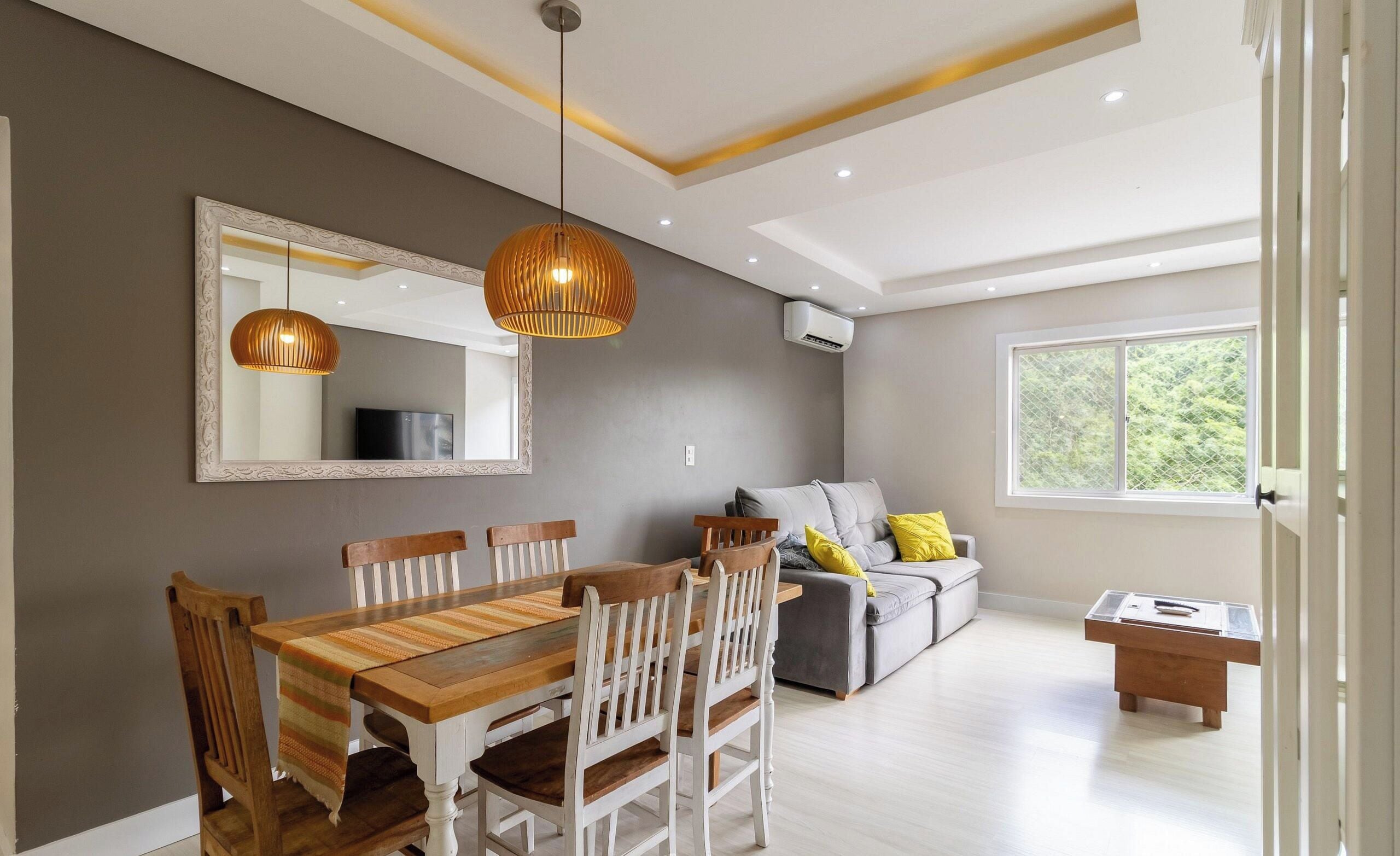 Una sala de estar moderna con comedor, paredes grises, un ventanal grande y un sofá gris con cojines amarillos.