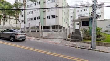 Un edificio de varios pisos con una entrada protegida por un portón, una escalera que conduce a la entrada y un coche estacionado en la calle.