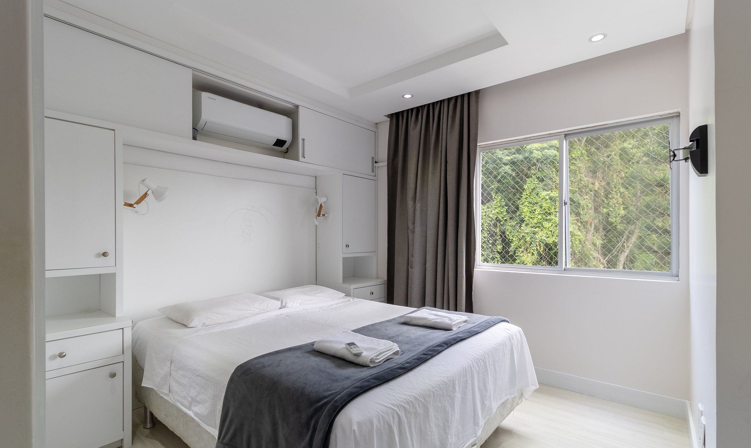 Un dormitorio moderno con una cama grande, almacenamiento integrado, una ventana con vistas a árboles y una lámpara de techo.