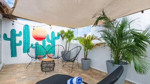 A sunlit patio with a cactus mural, lounge chairs, and potted plants. - Lovely 1BR Penthouse, Private pool, fast wifi (Playa del Carmen)