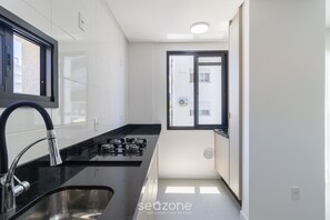 Cocina moderna con estufa a gas, pileta de acero inoxidable y ventana con vista al exterior.