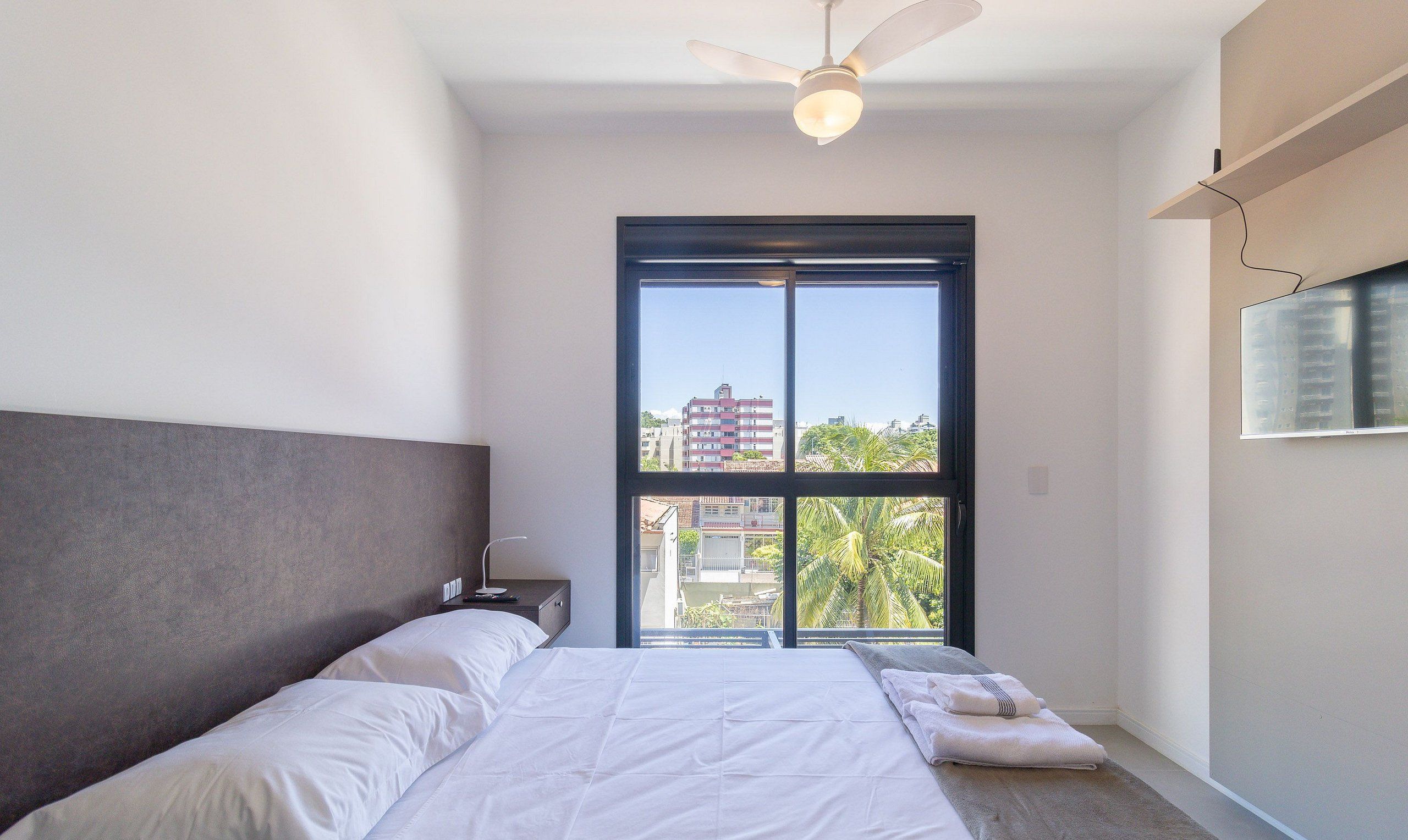 A bedroom with a large window, a ceiling fan, and a bed with white linens.