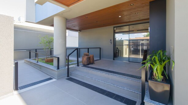A modern building entrance with a wooden ceiling, a glass door, and a small outdoor seating area with steps and a planter. - Modern Studio 650m From Ufsc - Cnt303 (Florianópolis)