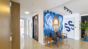 A modern lobby with a blue mural, a wooden door, a reception desk, and a potted plant. - Modern Studio 650m From Ufsc - Cnt303 (Florianópolis)