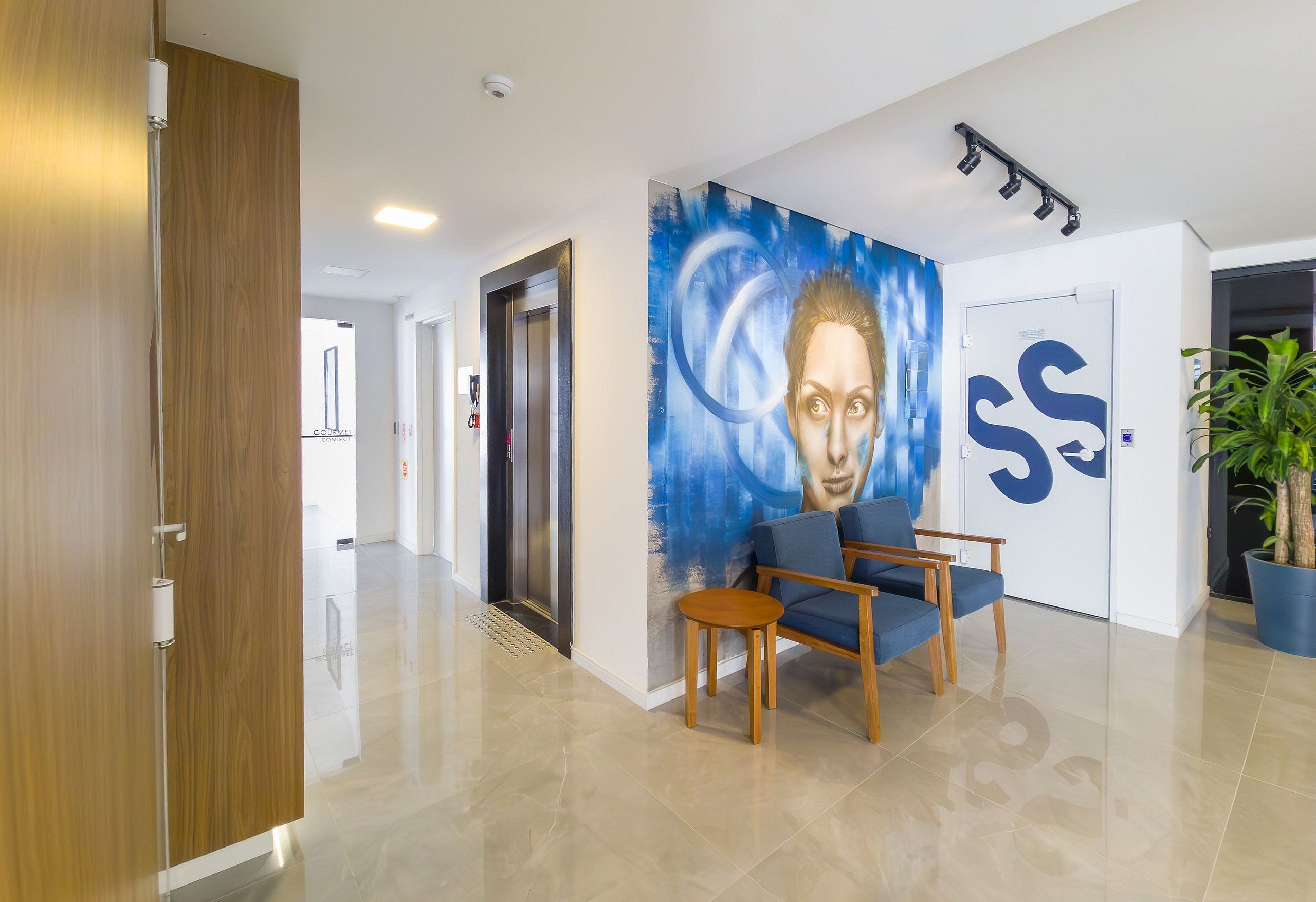 Un vestíbulo moderno con un mural azul, una puerta de madera, un mostrador de recepción y una planta en maceta.