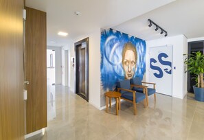 A modern lobby with a blue mural, a wooden door, a reception desk, and a potted plant. - Modern Comfort 650m From Ufsc - Cnt303 (Florianópolis)