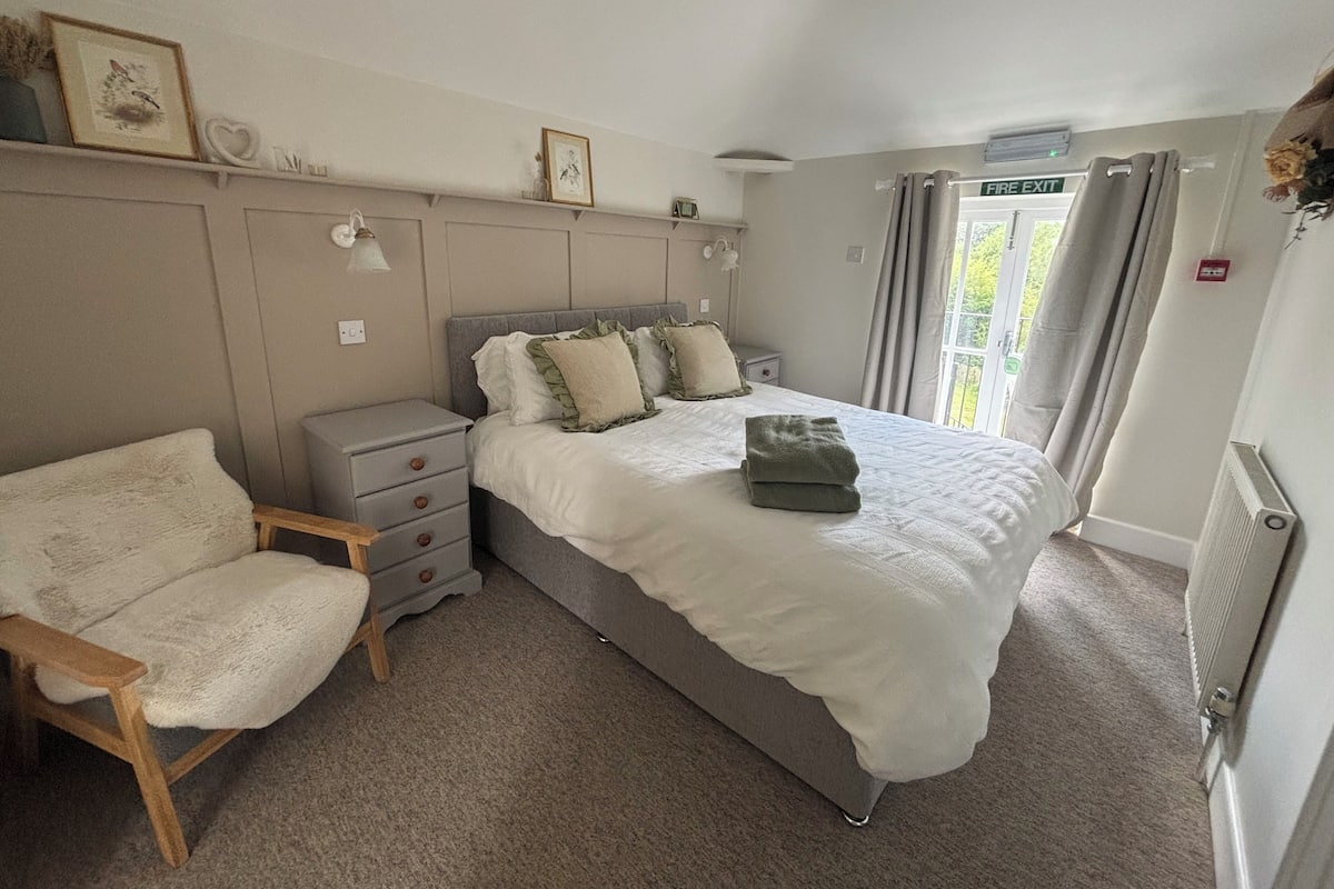 A bedroom with a bed, a chair, a nightstand, and a window with curtains.