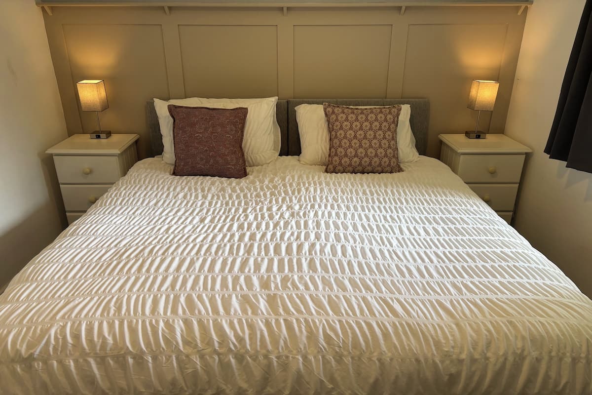A neatly made bed with a textured white duvet, two decorative pillows, and two bedside lamps on matching nightstands.