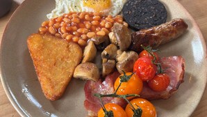 Un plato de comida para el desayuno con huevos, frijoles, champiñones, tocino, tomates y tostadas.