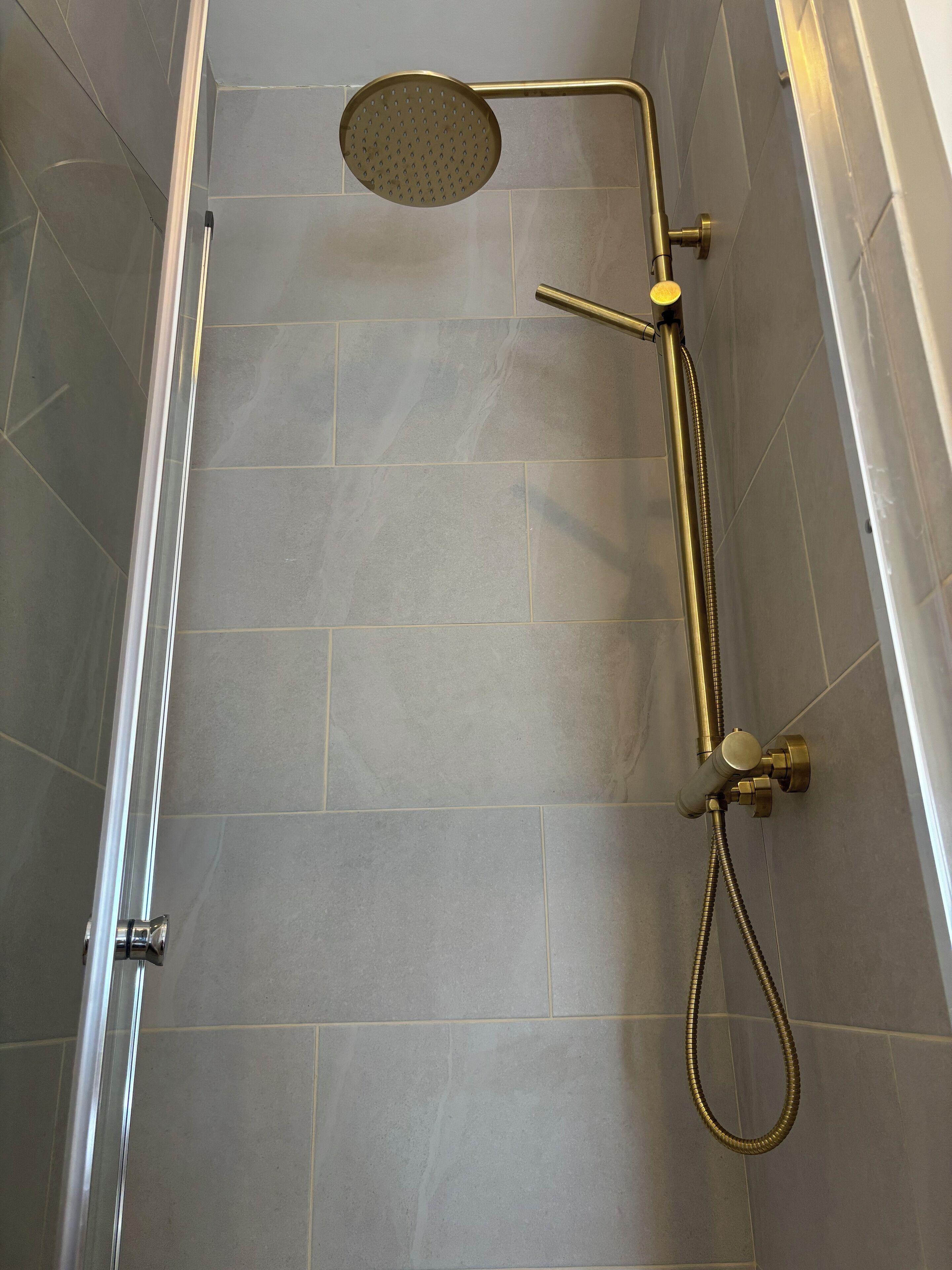 A shower with a handheld showerhead and a wall-mounted faucet.