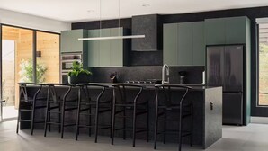 Eine moderne Küche mit einer zentralen Kochinsel, Barhocker, einem Kühlschrank und einem großen Fenster.