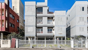 A multi-story residential building with balconies, a gated entrance, and a clear blue sky.