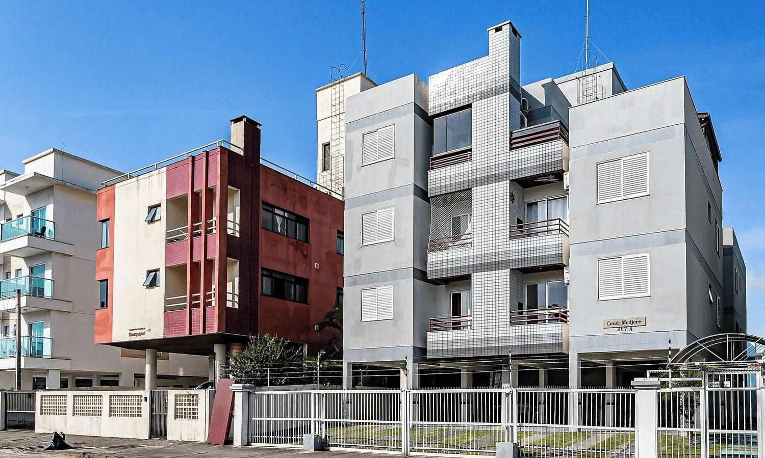 Un edificio moderno de varios pisos con balcones, entrada protegida y cielo despejado.