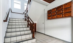 Een trap met houten leuningen en een betegelde vloer, die leidt naar een kamer met een wandrek.