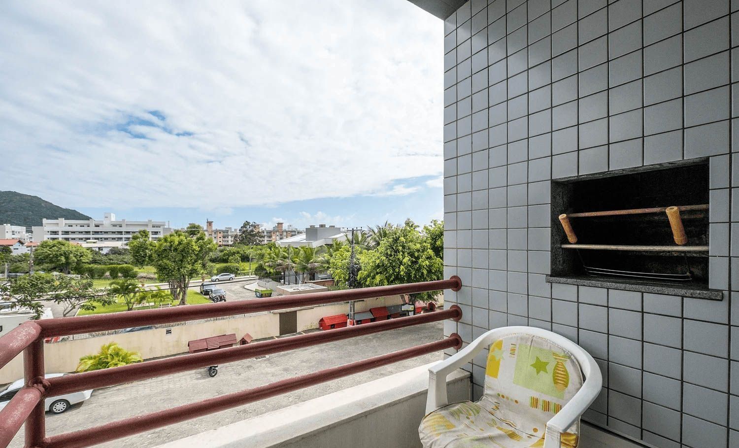 Balkon med udsigt over parkeringsplads og bygninger, en flisevæg og et lille vindue.