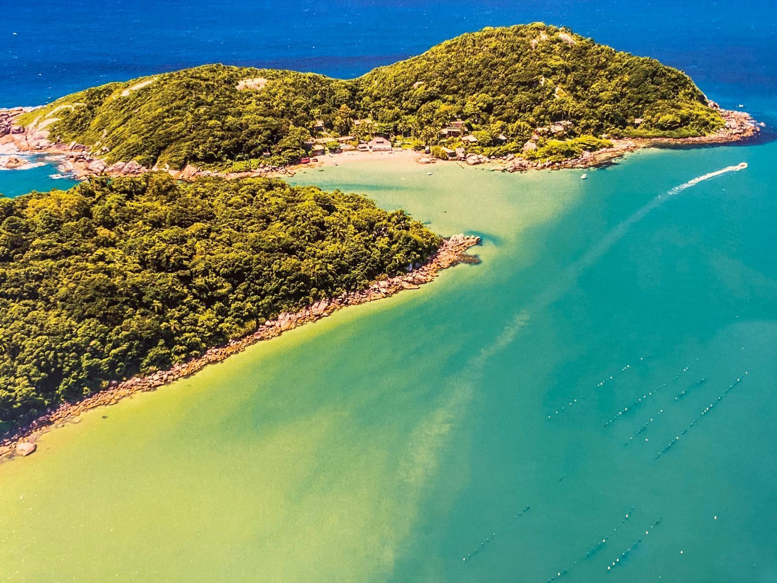 Une vue aérienne d’une zone côtière avec deux îles verdoyantes et boisées, reliées par une étroite bande de terre.