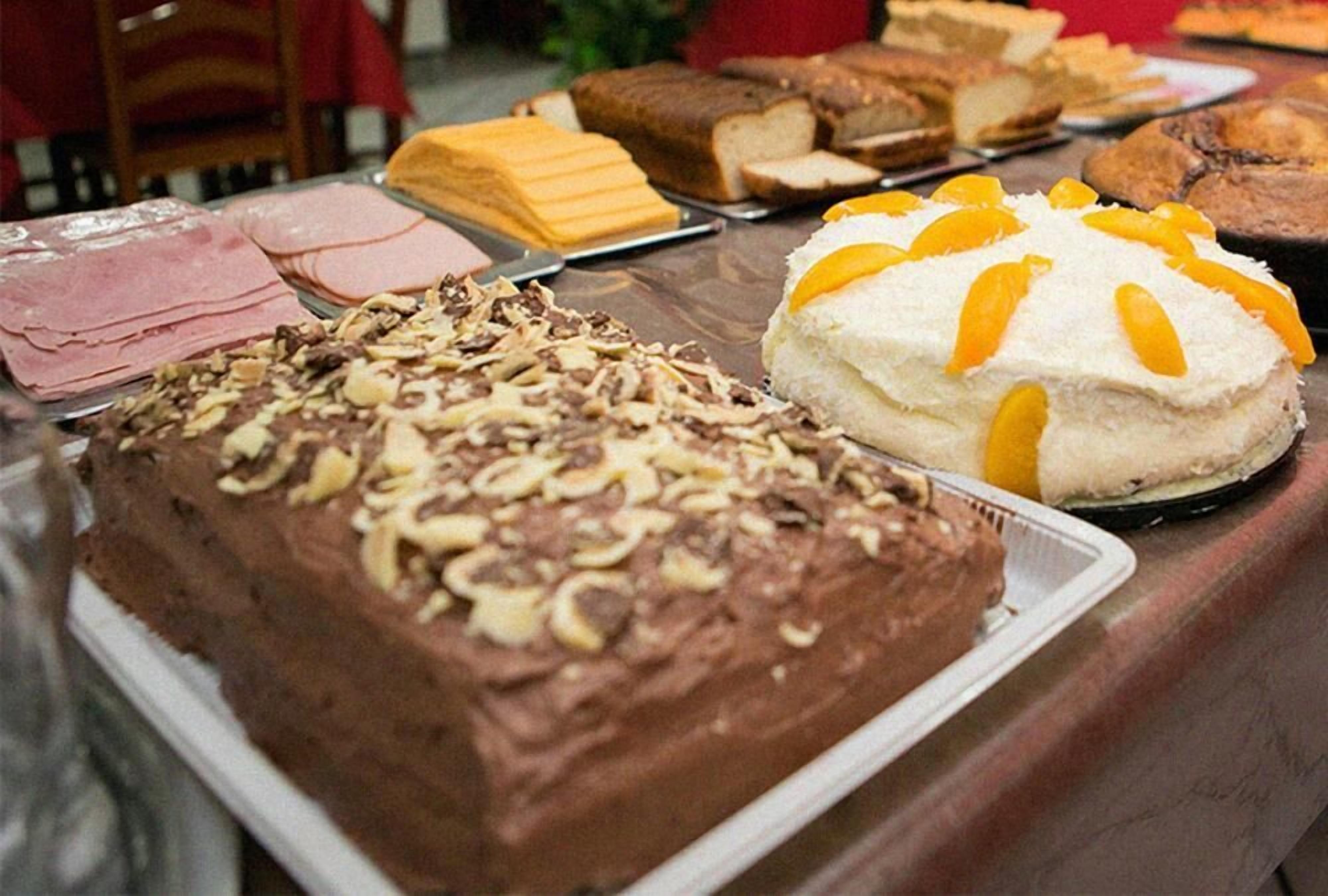 A variety of desserts on a table, including a chocolate cake with nuts, a white cake with orange slices, and several other baked goods.