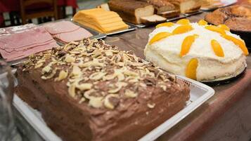 A variety of desserts on a table, including a chocolate cake with nuts, a white cake with orange slices, and several other baked goods.