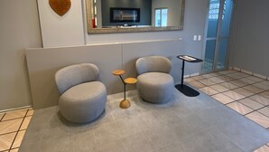 Een moderne woonkamer met een grote spiegel, twee ronde grijze banken, een klein bijzettafeltje en een klok aan de muur.