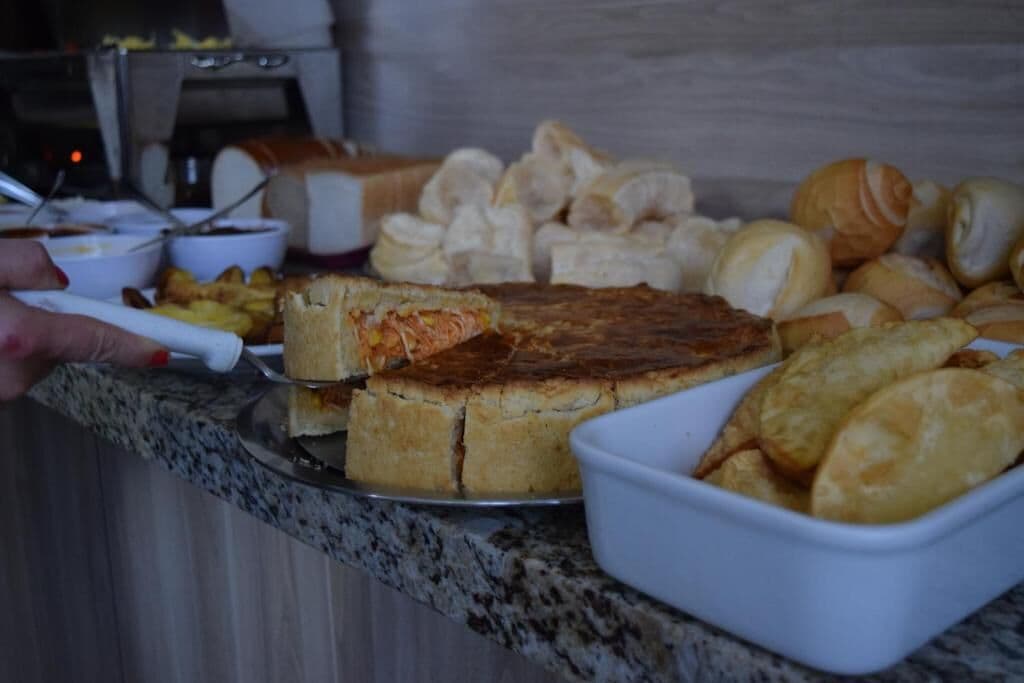 A buffet with various food items including bread, pastries, and a slice of cake being served.