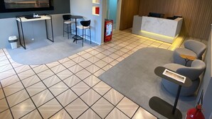 Een moderne hotellobby met een receptiebalie, een zithoek en een groot scherm waarop een stadsbeeld te zien is.