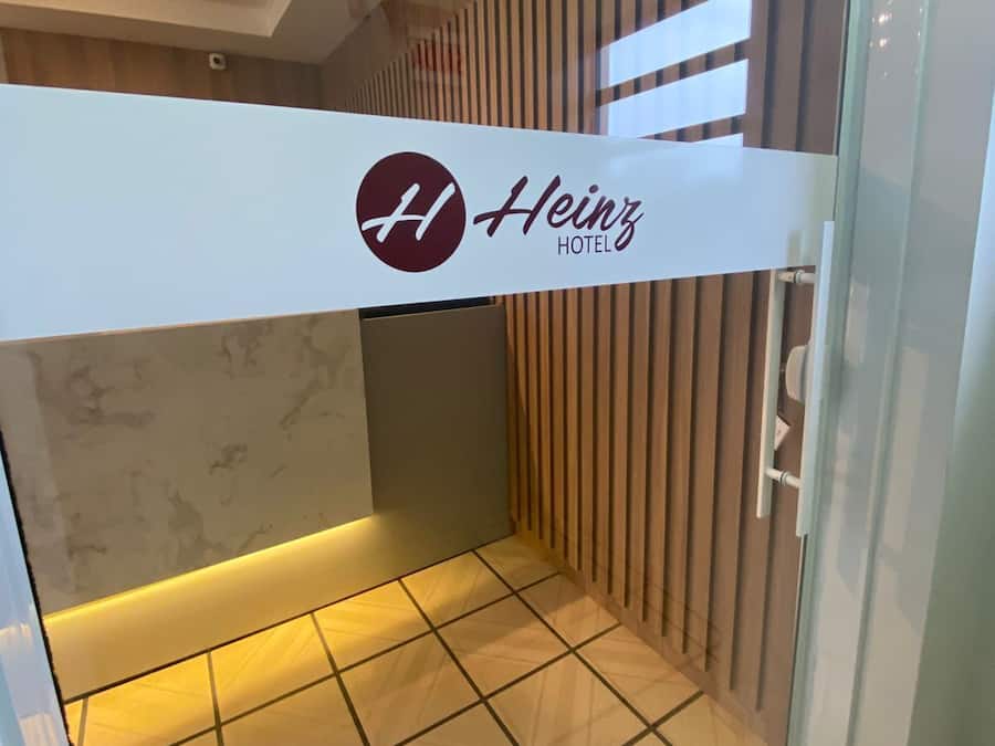 Un'area reception di un hotel con un cartello che indica 'Heinz Hotel' e un design moderno caratterizzato da pannelli in legno e pavimento piastrellato.